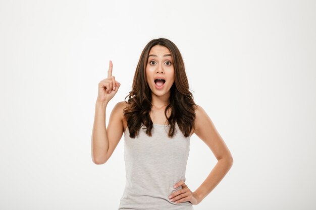 Surprised brunette woman with arm on hip having idea and looking at th camera over gray