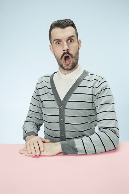 Surprised business man sitting at table on blue  space