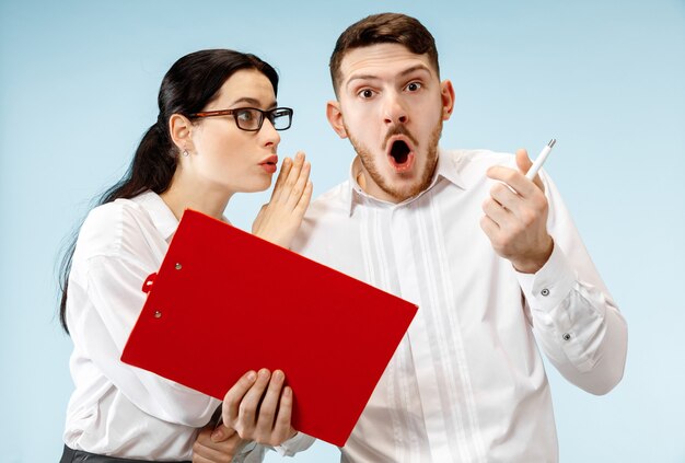 The surprised business man and woman smiling on a blue studio background