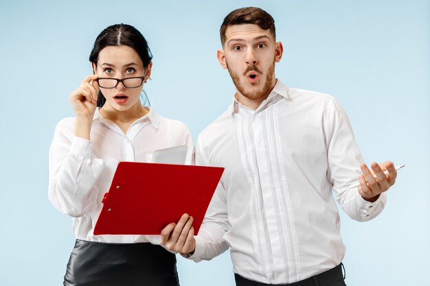 The surprised business man and woman smiling on a blue studio wall