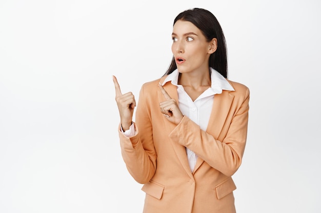 Surprised businesswoman looking at diagram Saleswoman in suit pointing at upper left corner standing over white background