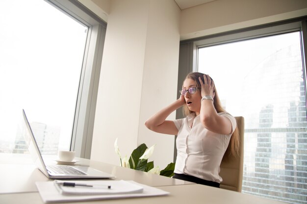 Surprised businesswoman sitting with head in hands