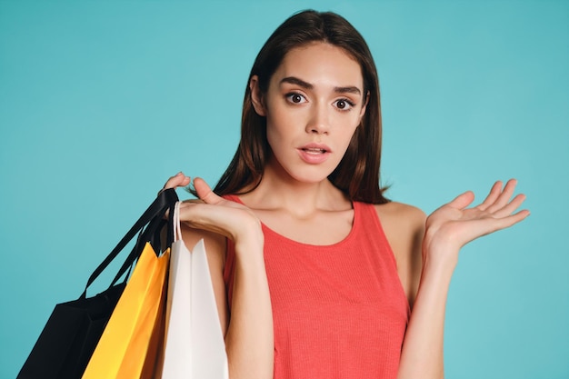 Удивленная случайная девушка с сумками для покупок задумчиво смотрит в камеру на красочном изолированном фоне