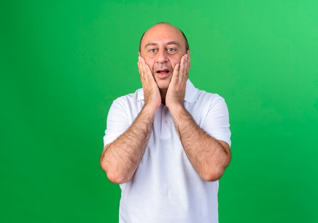 Surprised casual mature man covered face with hands isolated on green wall
