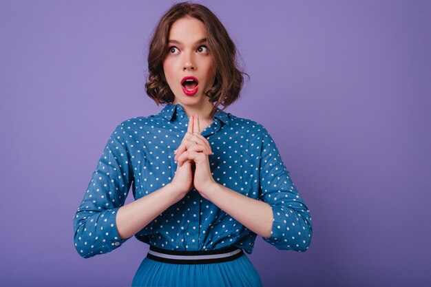 Surprised caucasian girl with brown eyes funny posing  Adorable short-haired lady in bright blouse isolated on purple wall.