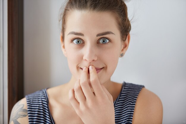 Surprised Caucasian woman with beautiful blue eyes and perfect white skin covering her mouth in curiosity with astonishment. Young girl overwhelmed with joy, totally shocked by good unexpected news.