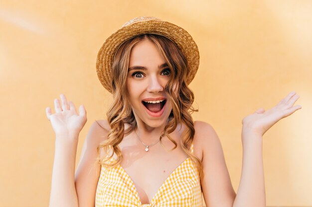 Surprised caucasian woman with wavy hairstyle posing in trendy hat. Portrait of debonair girl isolated.