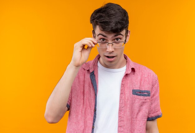 Surprised caucasian young guy wearing pink shirt in glasses on isolated orange background