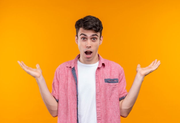 Surprised caucasian young guy wearing pink shirt spreads hands on isolated orange background