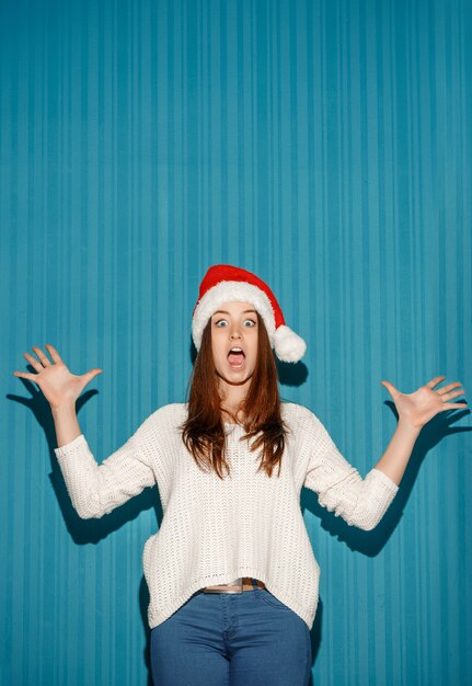 The surprised christmas girl wearing a santa hat on the blue background