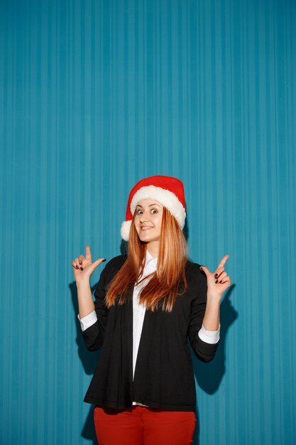 블루 스튜디오 배경에 산타 모자를 쓰고 놀란 크리스마스 소녀