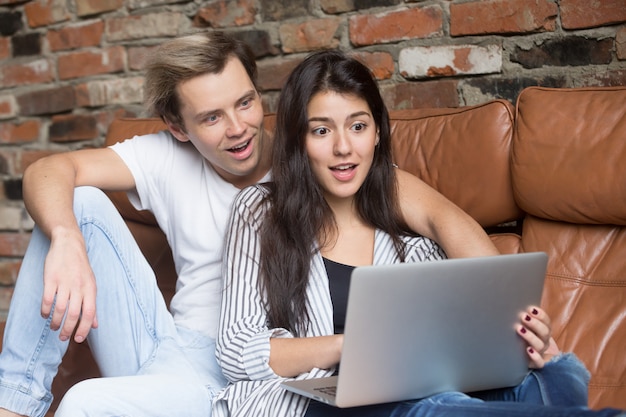 Surprised couple looking at laptop amazed by unbelievable online offer