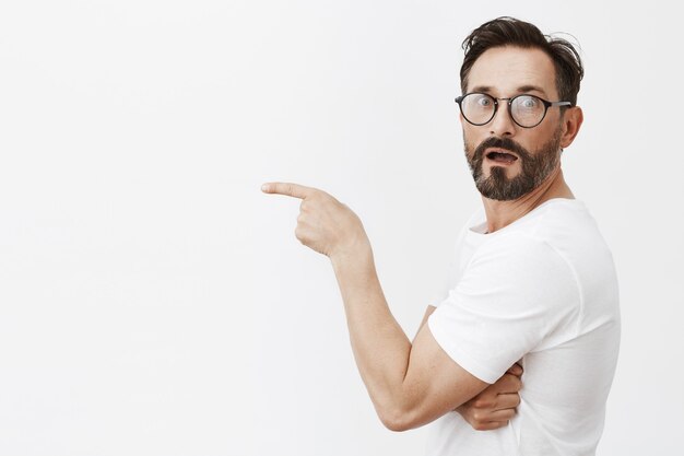 眼鏡をかけてポーズをとって驚いて好奇心旺盛なひげを生やした成熟した男