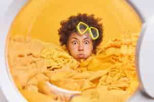 Free photo surprised curly haired young woman stares shocked at camera drowned in laundry