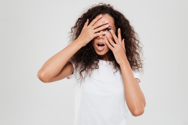 Surprised curly woman covering her face