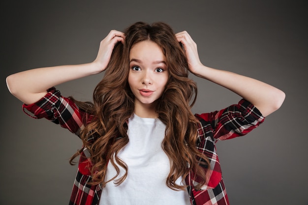 Surprised curly young woman standing with hands on head