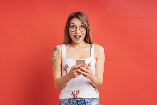 Surprised cute girl with a phone in hands on red wall 