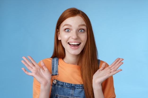 Surprised delighted happy friendly-looking amused redhead female friend learn incredible good news congratulating girlfriend fascinated wide eyes camera joyfully clap hands amazed, blue background.