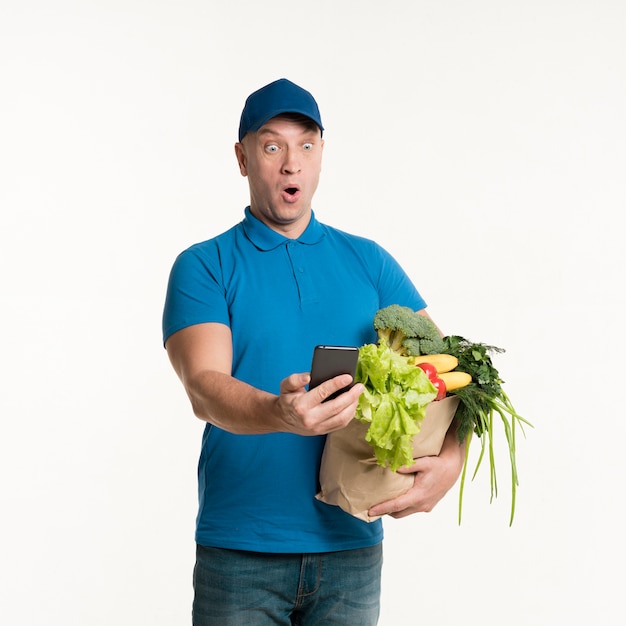 Surprised delivery man looking at phone while holding grocery bag