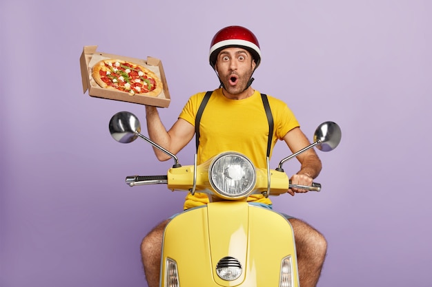 Fattorino sorpreso alla guida di scooter giallo mentre si tiene la scatola della pizza