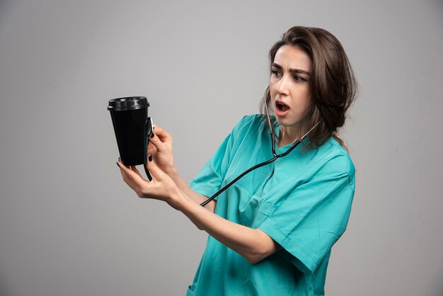 Surprised doctor checking coffee cup with stethoscope. High quality photo