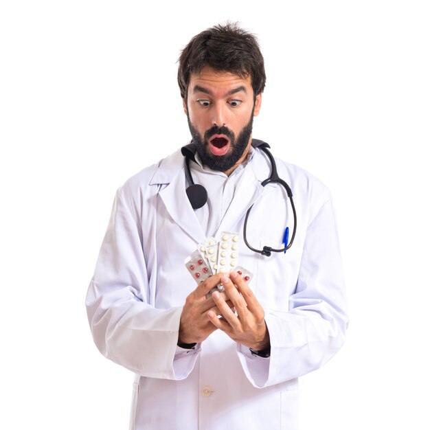 Surprised doctor holding pills over white background