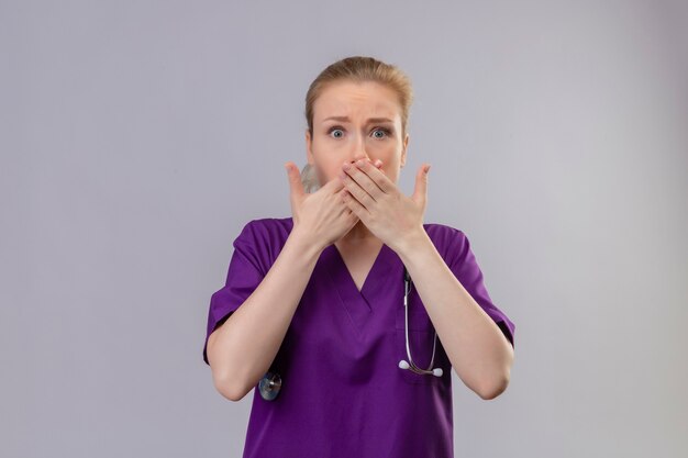 Surprised doctor young girl wearing purple medical gown and stethoscope covered mouth on isolated white background