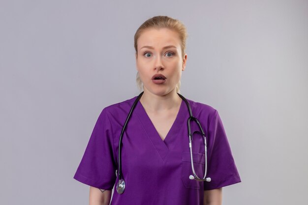 Surprised doctor young girl wearing purple medical gown and stethoscope on isolated white background