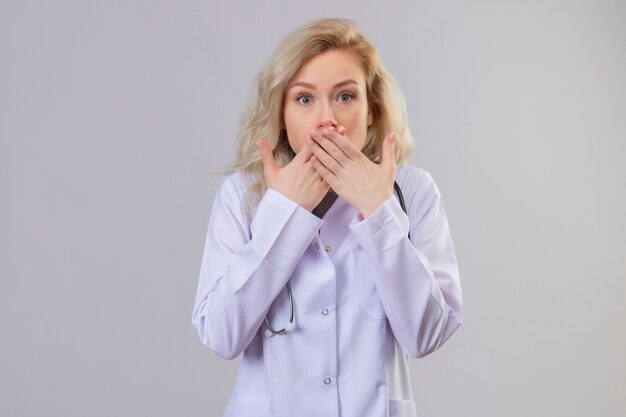 Surprised doctor young girl wearing stethoscope in medical gown covered mouth on white background