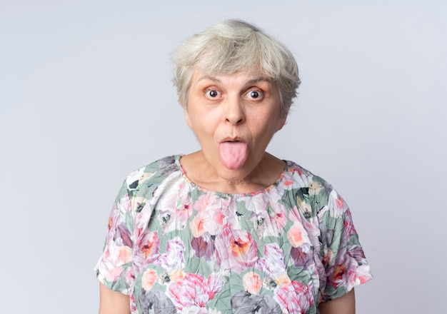 Free photo surprised elderly woman sticks out tongue isolated on white wall