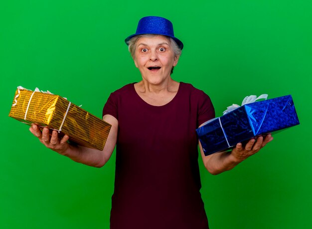 파티 모자를 쓰고 놀란 된 노인 여성 녹색에 선물 상자를 보유