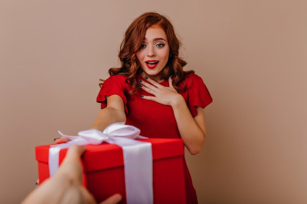 Surprised elegant woman looking at new year present. Indoor portrait of glamorous girl enjoying christmas time.