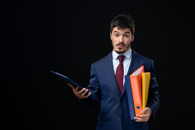 Surprised emotional adult in suit holding several documents on isolated dark wall