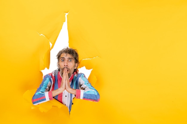 Surprised and emotional young man poses in torn yellow paper hole background