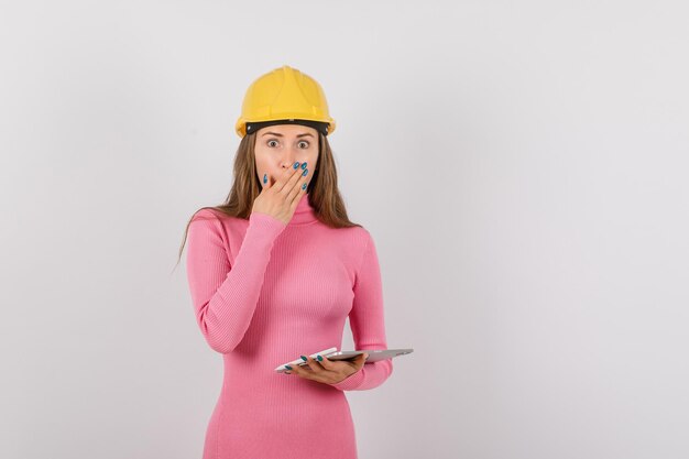 Surprised engineer girl is holding hand on mouth by holding tablet computer on white background