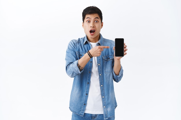 Удивленный и взволнованный азиатский парень показывает друзьям профиль человека, сопоставленного с ним в приложении для знакомств, потрясенный и потрясенный, указывая на смартфон