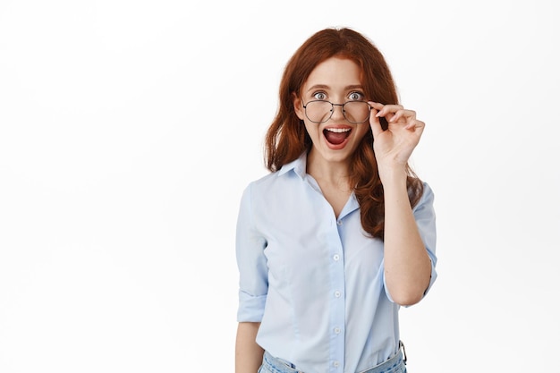 Surprised and excited businesswoman, office lady takes off glasses and drops jaw from amazing news, super cool promotion offer, taking look at great discounts, white background