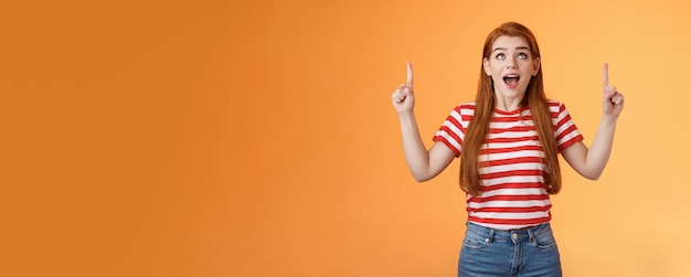 Free photo surprised excited cheerful ginger girl see amazing opportunity look pointing up amused drop jaw gasp