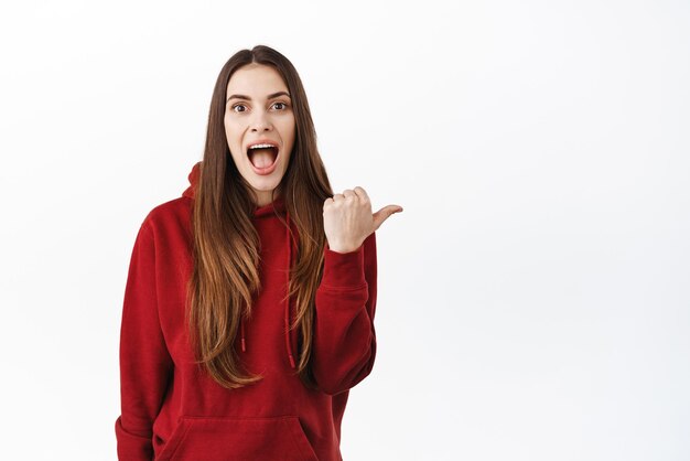 Surprised and excited girl checking out awesome promo deal best offer in store pointing aside at right copy space and drop jaw fascinated staring at camera impressed white background