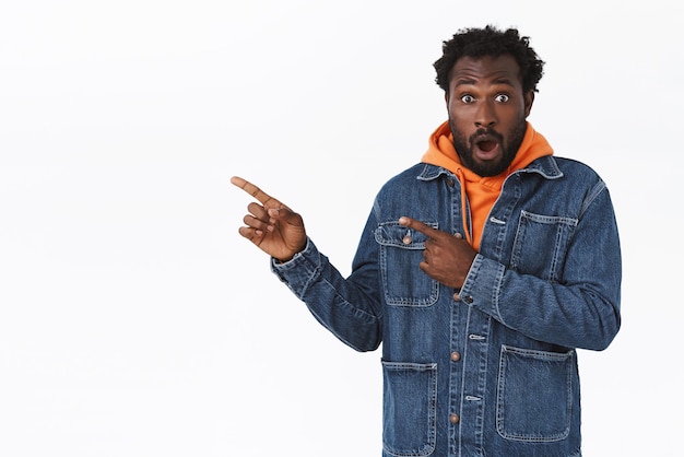Free photo surprised, excited handsome bearded african american male in denim jacket, autumn orange hoodie, gasping amazed, drop jaw speechless