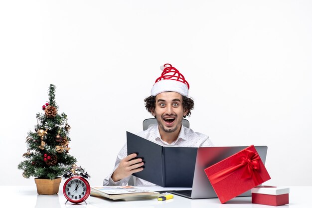 Surprised excited positive young businessman with funny santa claus hat checking information in documents in the office on white background