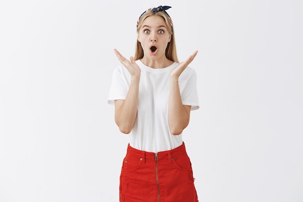 Surprised and excited young blond girl posing against the white wall