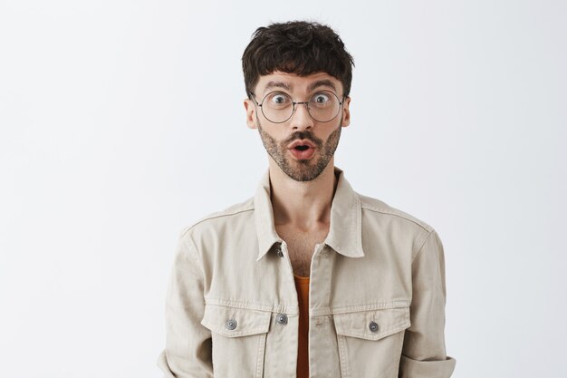 Surprised and fascinated stylish bearded guy posing against the white wall