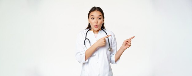 Surprised female doctor say wow pointing right and looking amazed with discounts in clinic showing w