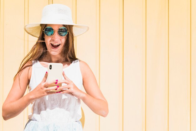 Free photo surprised female standing near wooden wall with smartphone