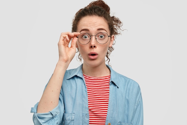 Surprised freckled girl looks in bewilderment at camera, reacts on unexpected news