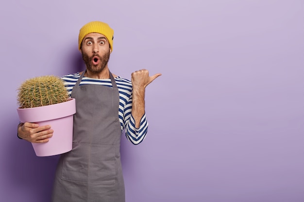 Free photo surprised gardener posing with a big  potted cactus