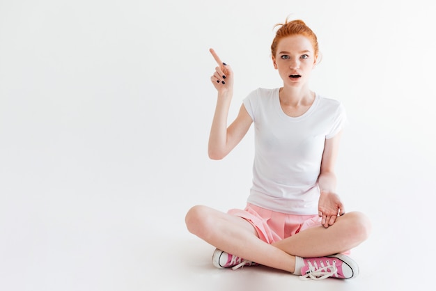 Surprised ginger girl sitting on the floor and looking while pointing away