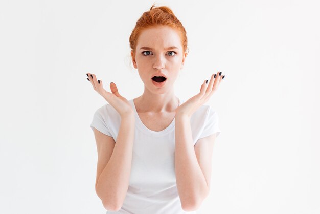 Surprised ginger woman in t-shirt looking with hands near the head