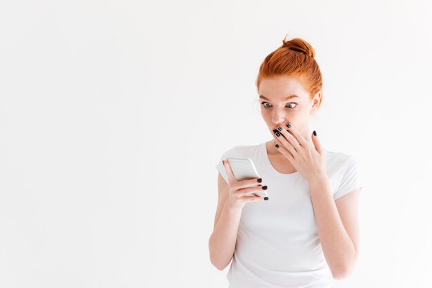Surprised ginger woman in t-shirt using her smartphone